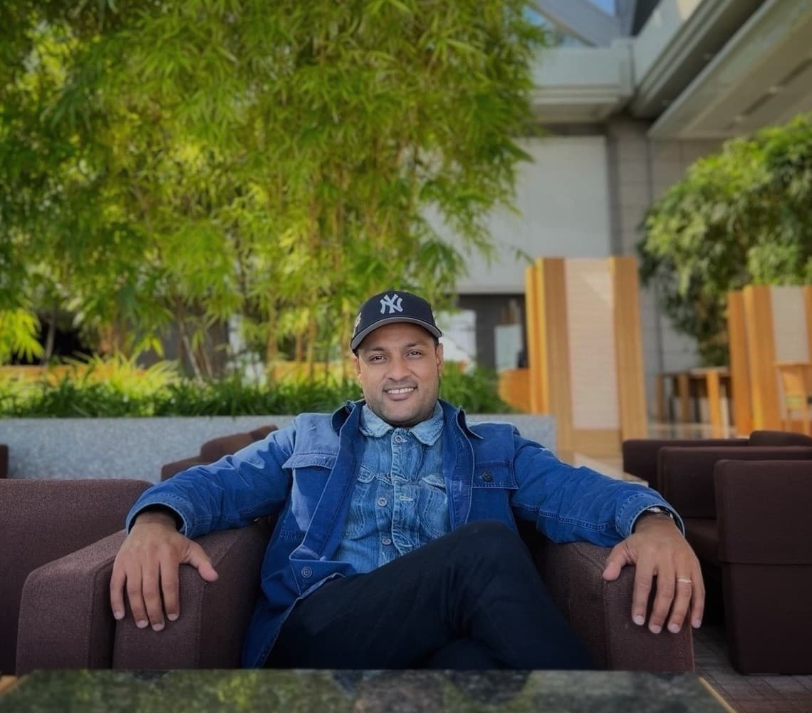 Drew Nagda seated outdoors in a denim jacket and Yankees cap